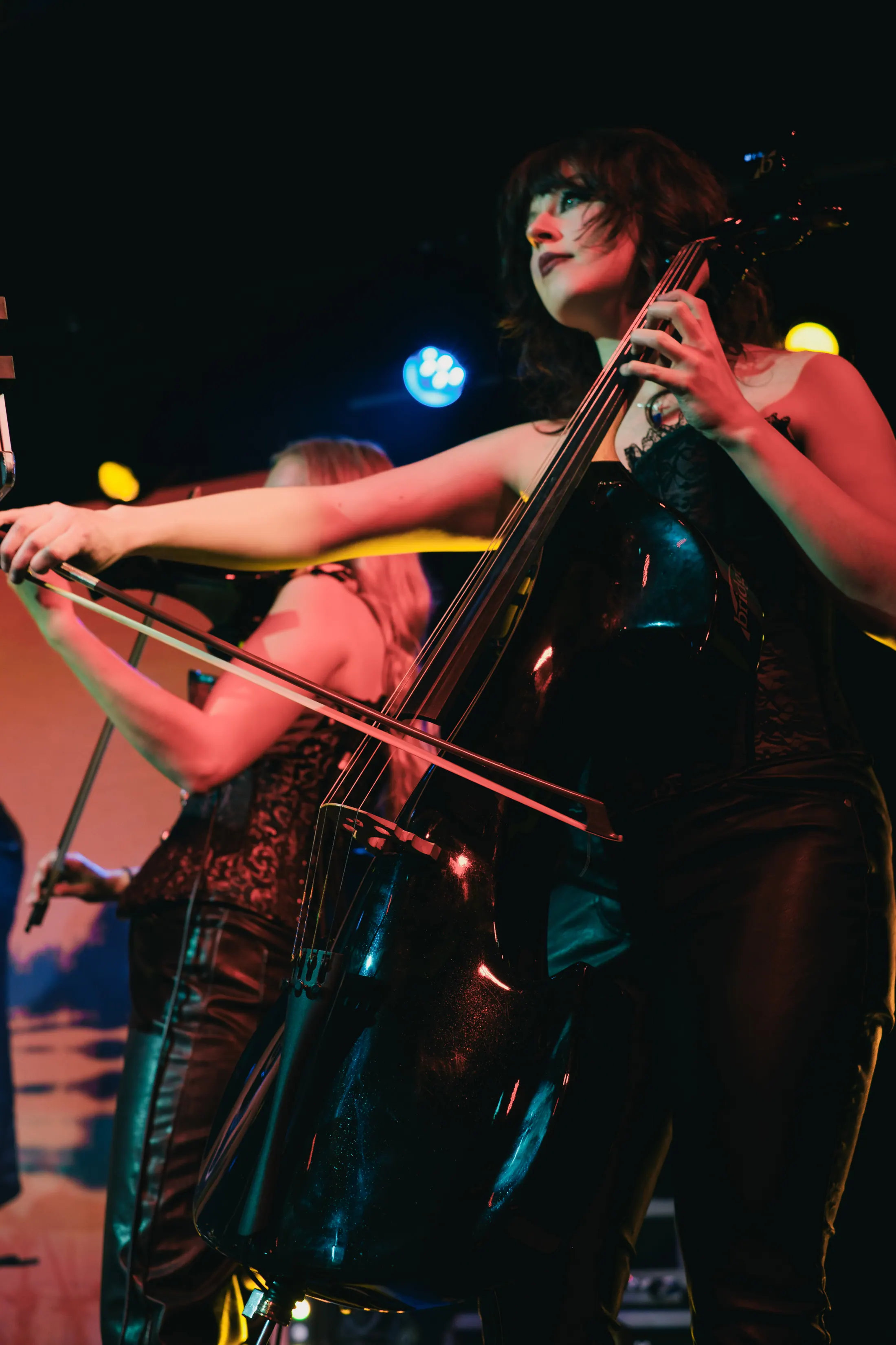 An In Symphony cellist performing under stage lighting